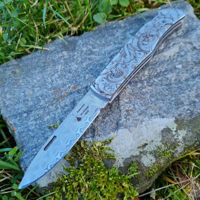 An Aquila lock back folding knife laid open on a mossy stone