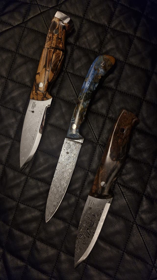 Three Damascus knives laid on dark quilted leather