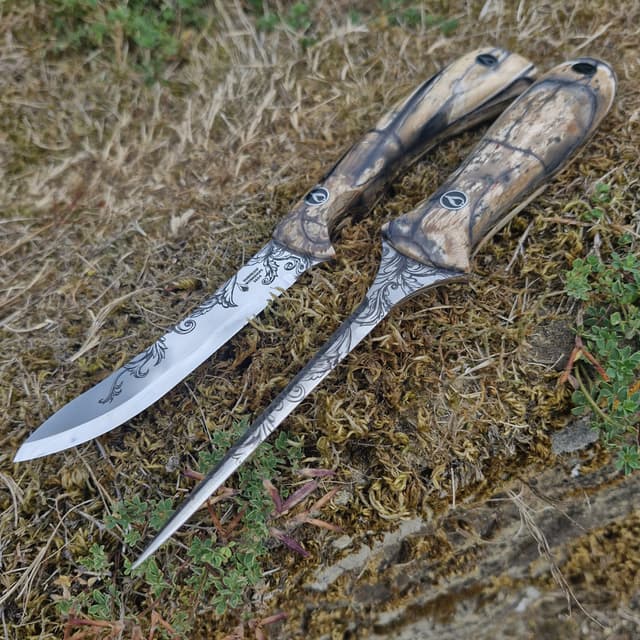 Two knives with scroll-etched blades and pale handles on moss