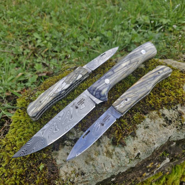 Three folding knives laid on a mossy rock