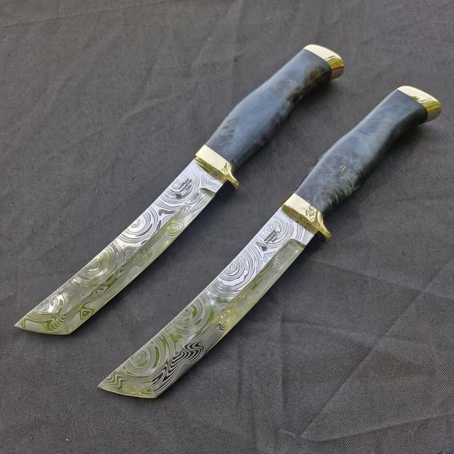 Two tanto-pointed knives with etched blades and brass guards on grey