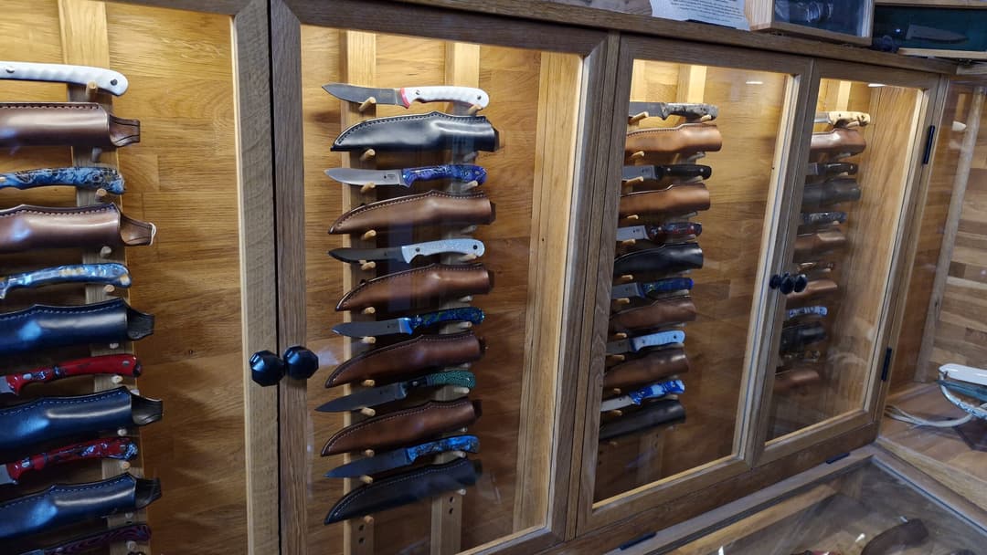 Showroom cabinet doors — rows of knives resting in their leather sheaths on oak pegs