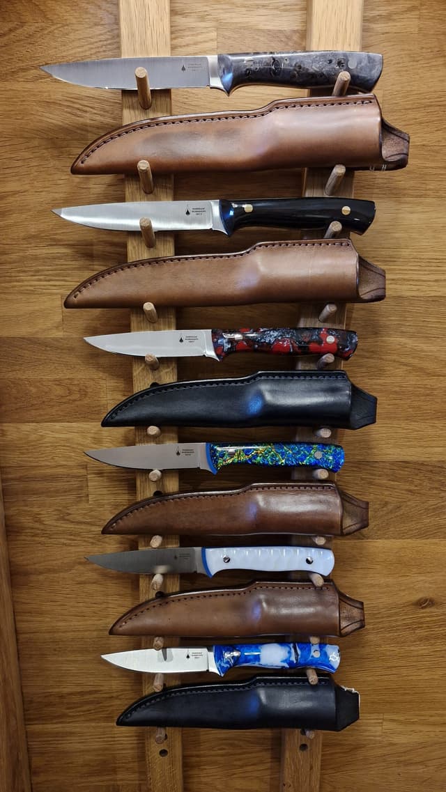Finished knives drawn from hand-made leather sheaths on a display rack
