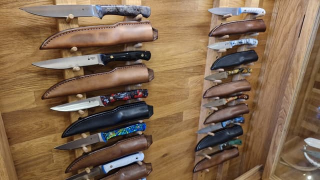 The showroom wall rack hung with finished knives in their sheaths
