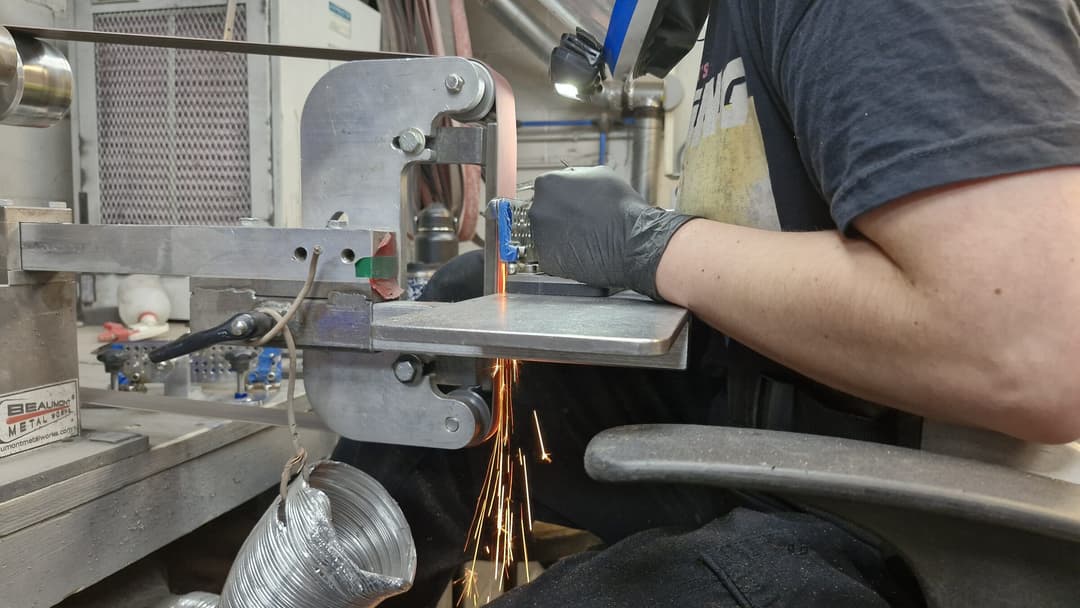 A maker grinding a blade at the belt grinder in the Emberleaf workshop