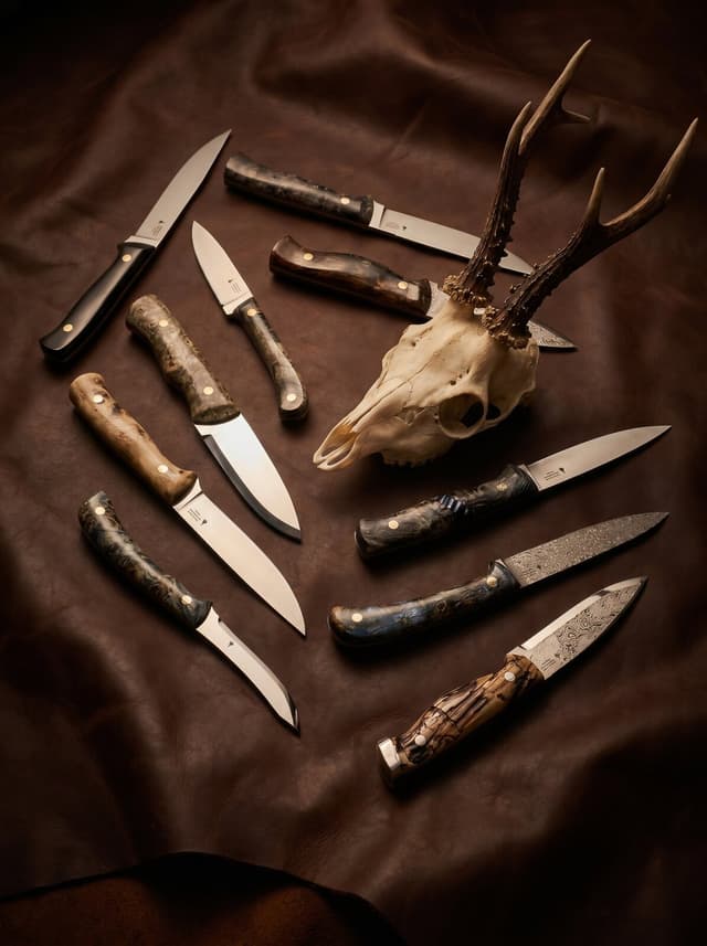 Hunting knives with burl and stag handles around a roe-deer skull on leather