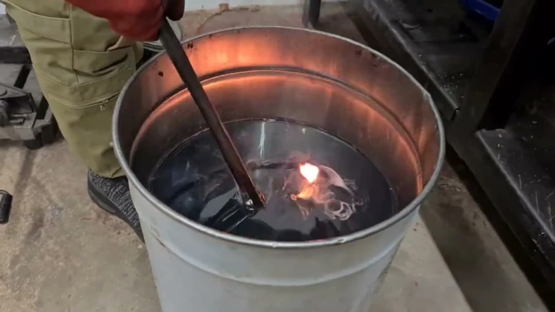 Quenching a hot blade in a tank of oil, bright orange flame on the surface