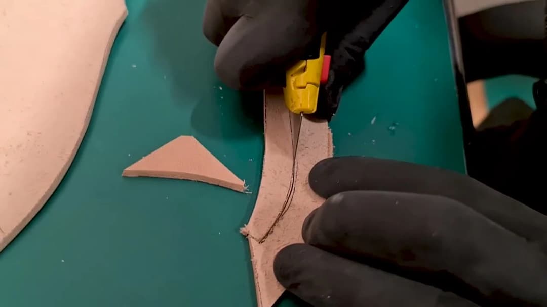 Cutting a leather sheath panel with a knife on a green cutting mat, pattern pieces beside