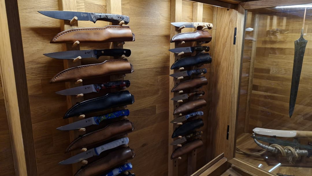 Sheathed Emberleaf knives racked inside the oak showroom cabinet